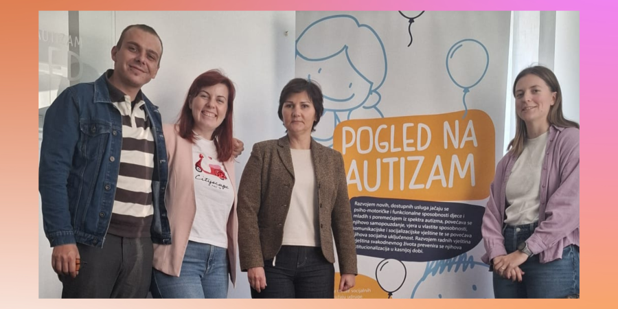 Četvero ljudi stoji u zatvorenom prostoru pokraj plakata na kojem piše „Pogled na autizam“. Plakat prikazuje ilustrirane balone i crtež nasmijanog djeteta. Skupina se smiješi i pozira za fotografiju.