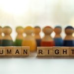 Fotografija zamućenih drvenih figurica za Čovjeće ne ljuti se igru. Ispred njih su od drvenih kocki sa slovima složene riječi Human Rights